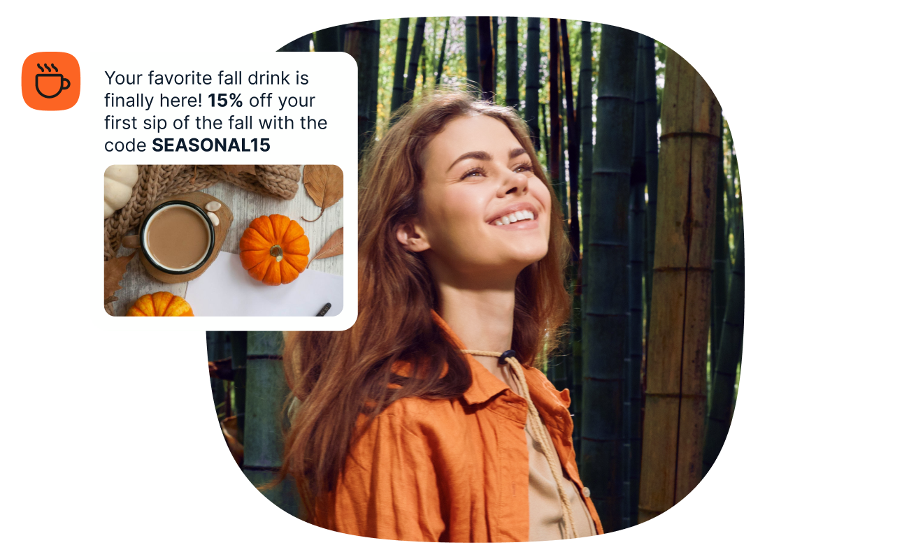 Smiling woman in an orange jacket standing in a bamboo forest, with an overlaid chat notification that reads: "Your favorite fall drink is finally here! 15% off your first sip of the fall with the code SEASONAL15," accompanied by a small photo of a pumpkin spice latte with mini pumpkins and a coffee cup icon.