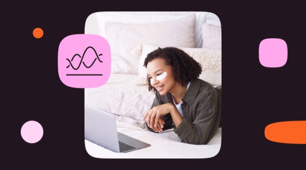 A woman with curly hair lies on a bed with white pillows and a knit blanket, wearing under-eye moisture patches and smiling at a laptop screen. A pink icon showing a stylized soundwave or pulse graphic sits in the top-left corner of the image, representing personalized, real-time engagement.