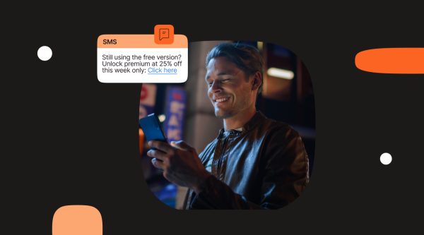Man smiling while reading promotional SMS offer on his phone with message text displayed: 'Still using the free version? Unlock premium at 25% off this week only: Click here