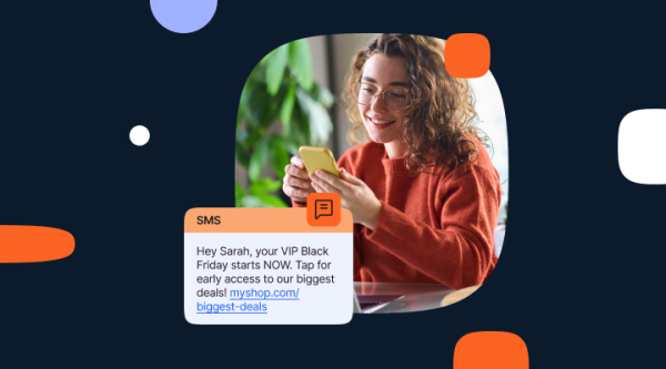 A young woman with curly brown hair and glasses, wearing an orange sweater, smiles while looking at her yellow smartphone. She is seated indoors with green plants blurred in the background. Overlaid on the image is an SMS mockup that reads: “Hey Sarah, your VIP Black Friday starts NOW. Tap for early access to our biggest deals! myshop.com/biggest-deals.” The design features rounded shapes in orange, blue, and white on a dark navy background.