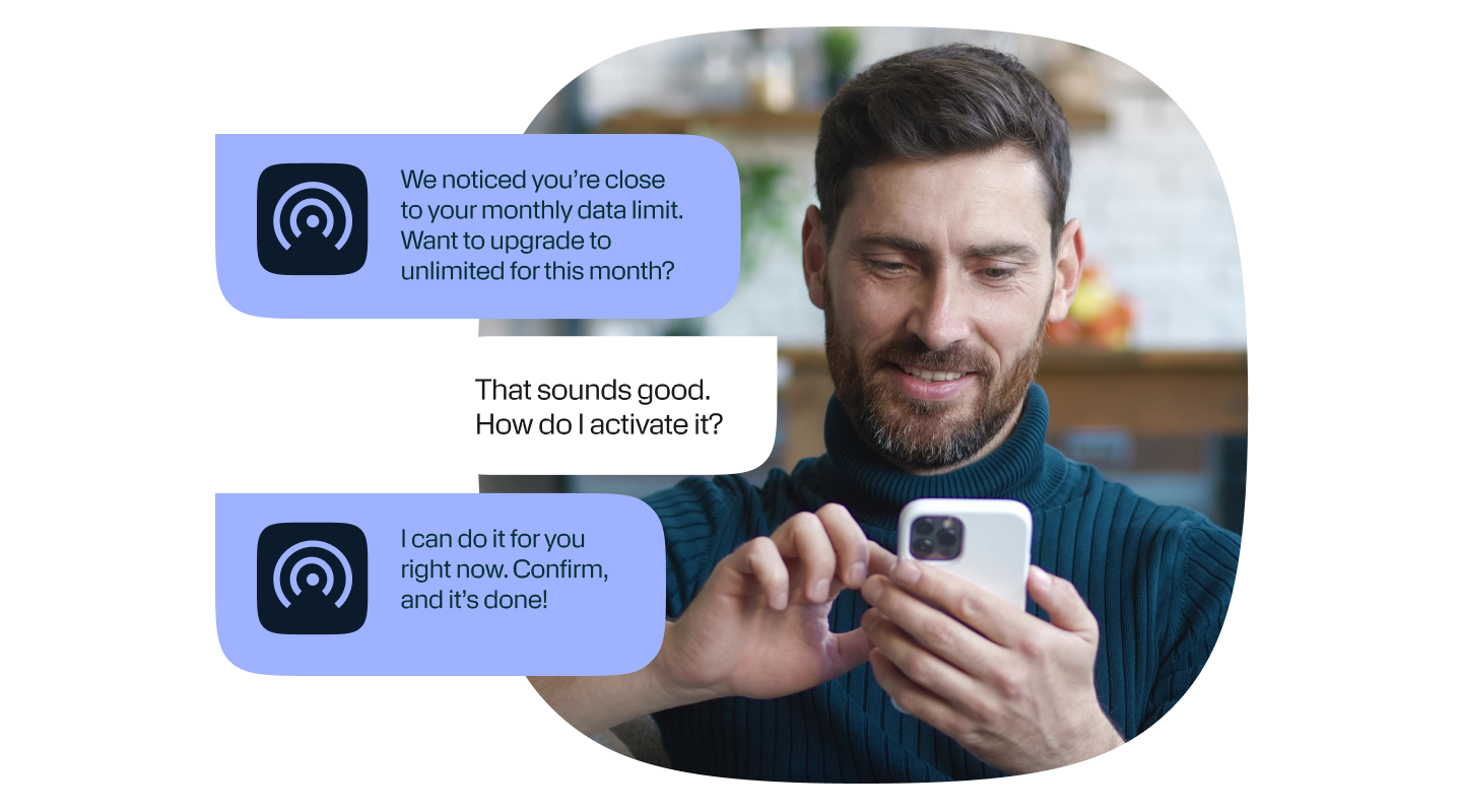 A man is interacting with a brand on the smartphone. Text message bubbles overlay the image: the first blue bubble says, "We noticed you’re close to your monthly data limit. Want to upgrade to unlimited for this month?" The white reply bubble says, "That sounds good. How do I activate it?" The second blue bubble says, "I can do it for you right now. Confirm, and it’s done!"