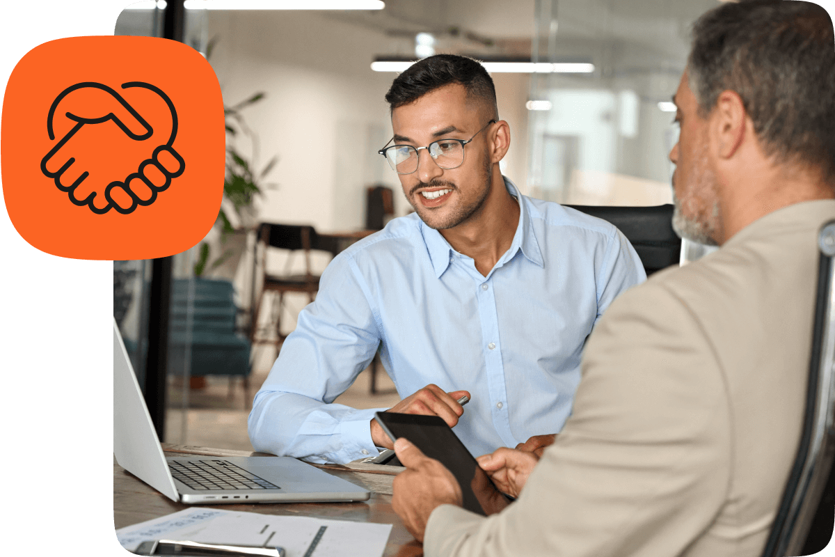 Two professionals in a modern office review a partnership proposal on a laptop and tablet; orange handshake icon indicates collaboration.