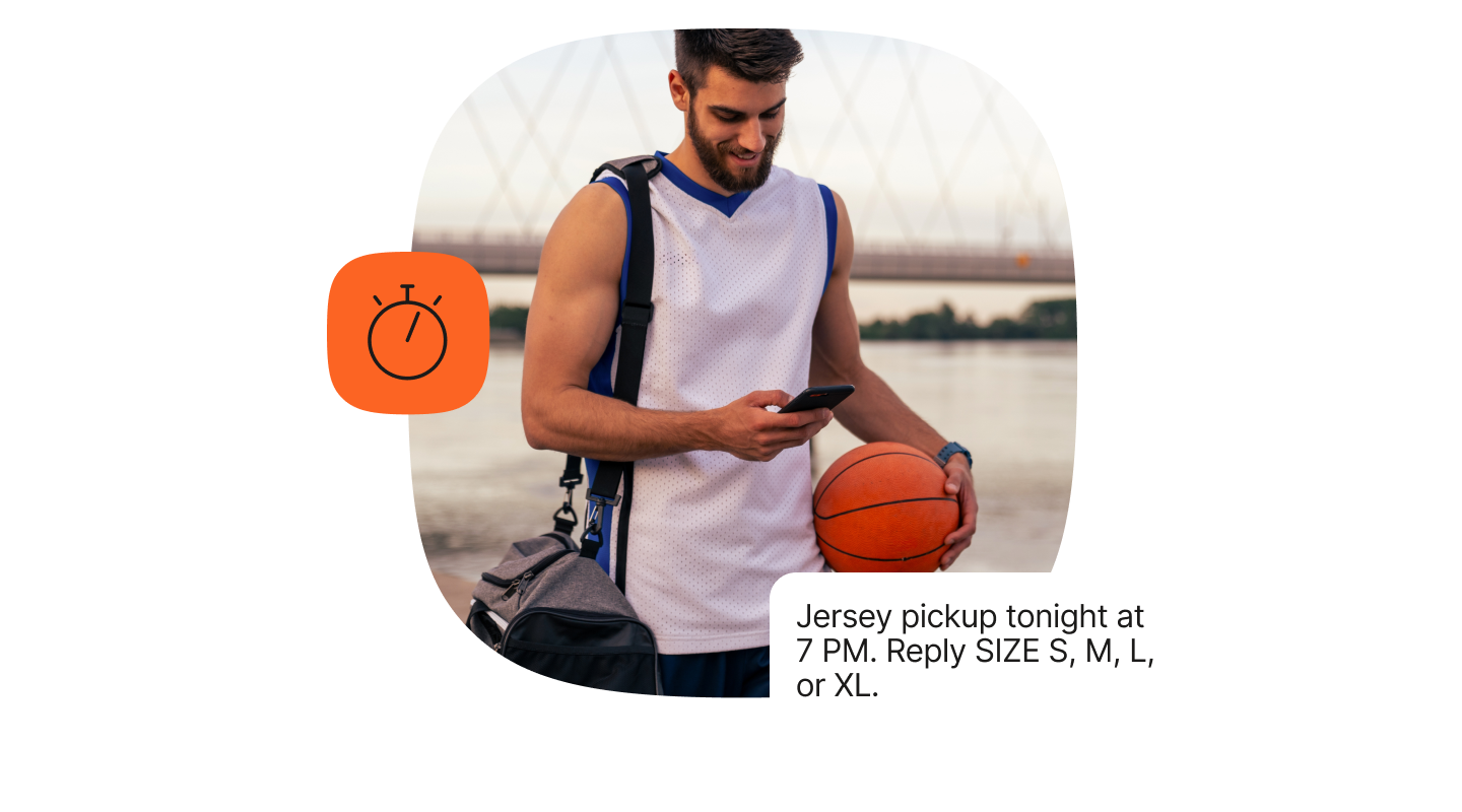A young man dressed in a white and blue sleeveless sports jersey is standing outdoors near a body of water with a bridge in the background. He is holding an orange basketball under one arm and looking at his phone with the other hand. A grey gym bag hangs over one shoulder, and he wears a digital sports watch on his wrist. To the left side of the image, an orange stopwatch icon appears next to a message about jersey pickup tonight at 7 PM, with instructions to reply with size S, M, L, or XL.