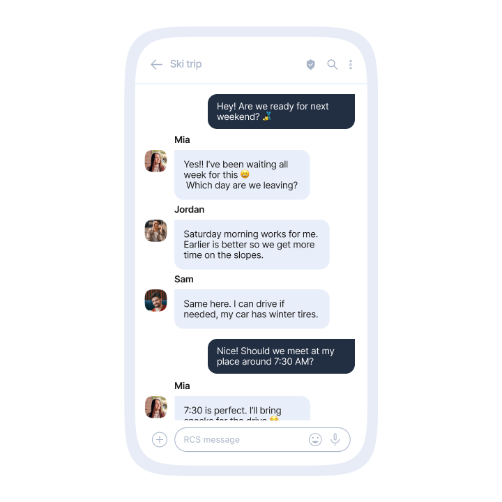 A smartphone screen displaying an RCS group chat titled ‘Ski trip.’ The conversation shows four participants with profile photos. The first message, in a dark blue bubble from the user, says: ‘Hey! Are we ready for next weekend? 🎉’. Mia replies in a light blue bubble: ‘Yes!! I’ve been waiting all week for this 😊 Which day are we leaving?’. Jordan follows with: ‘Saturday morning works for me. Earlier is better so we get more time on the slopes.’ Sam adds: ‘Same here. I can drive if needed, my car has winter tires.’ The user responds: ‘Nice! Should we meet at my place around 7:30 AM?’. Finally, Mia writes: ‘7:30 is perfect. I’ll bring snacks for the drive 😄.’ The bottom of the screen shows an RCS message input bar with icons for attachments, emojis, and sending.