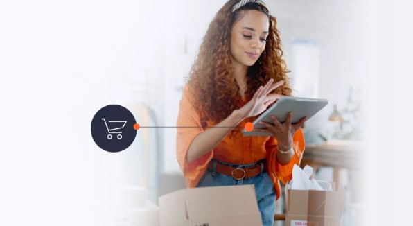 Una mujer con el pelo rizado está manipulando una tableta. Delante de ella hay cajas de compras.