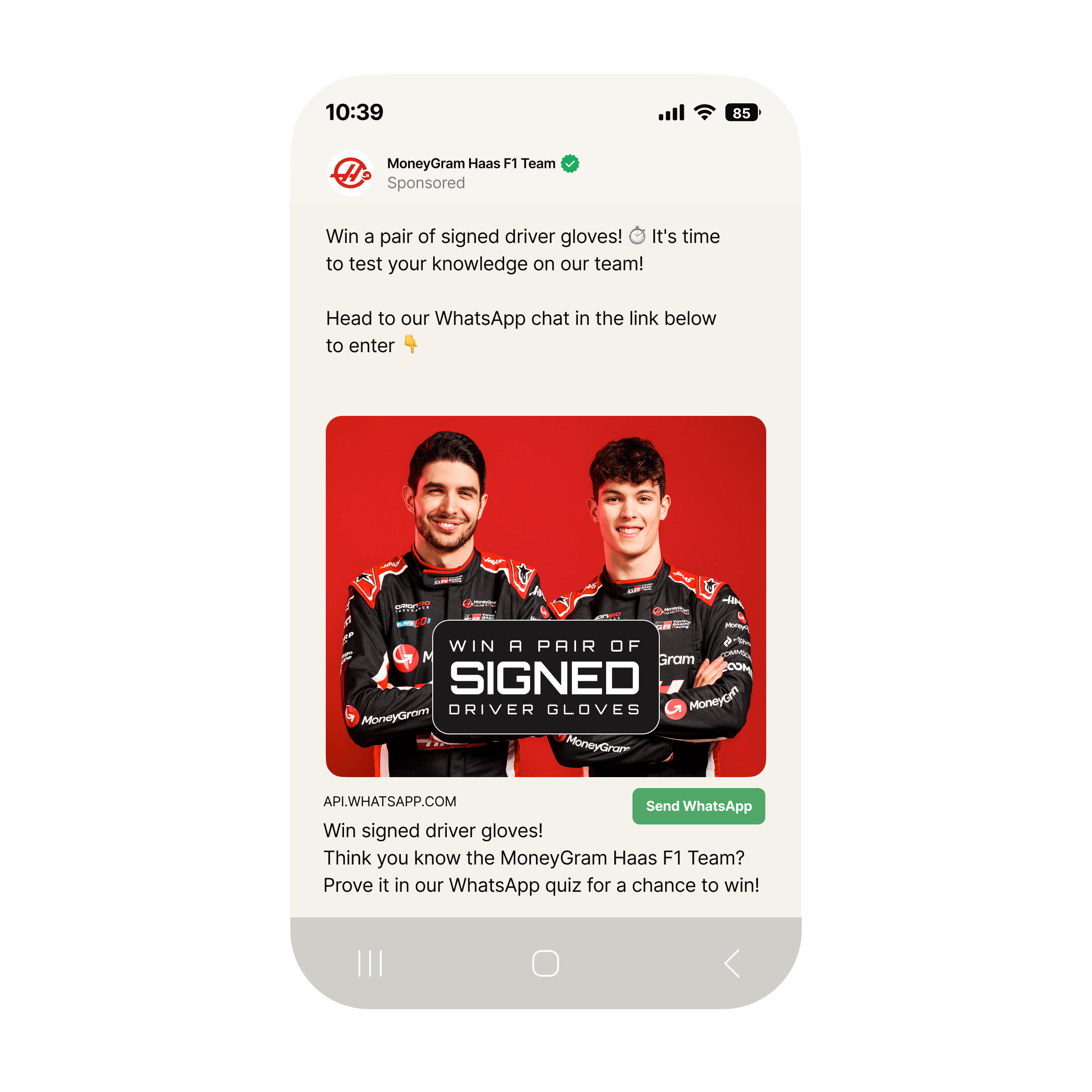 “Mobile phone screen showing a sponsored Facebook post from the MoneyGram Haas F1 Team promoting a WhatsApp quiz. The post invites users to ‘Win a pair of signed driver gloves’ by testing their knowledge of the team. Below the text is a red banner image featuring two Haas F1 drivers in black and red racing suits with sponsor logos, standing side by side. Over the banner is a bold black box with white text that reads ‘Win a pair of signed driver gloves.’ At the bottom of the post there is a button labeled ‘Send WhatsApp’ to enter the quiz.