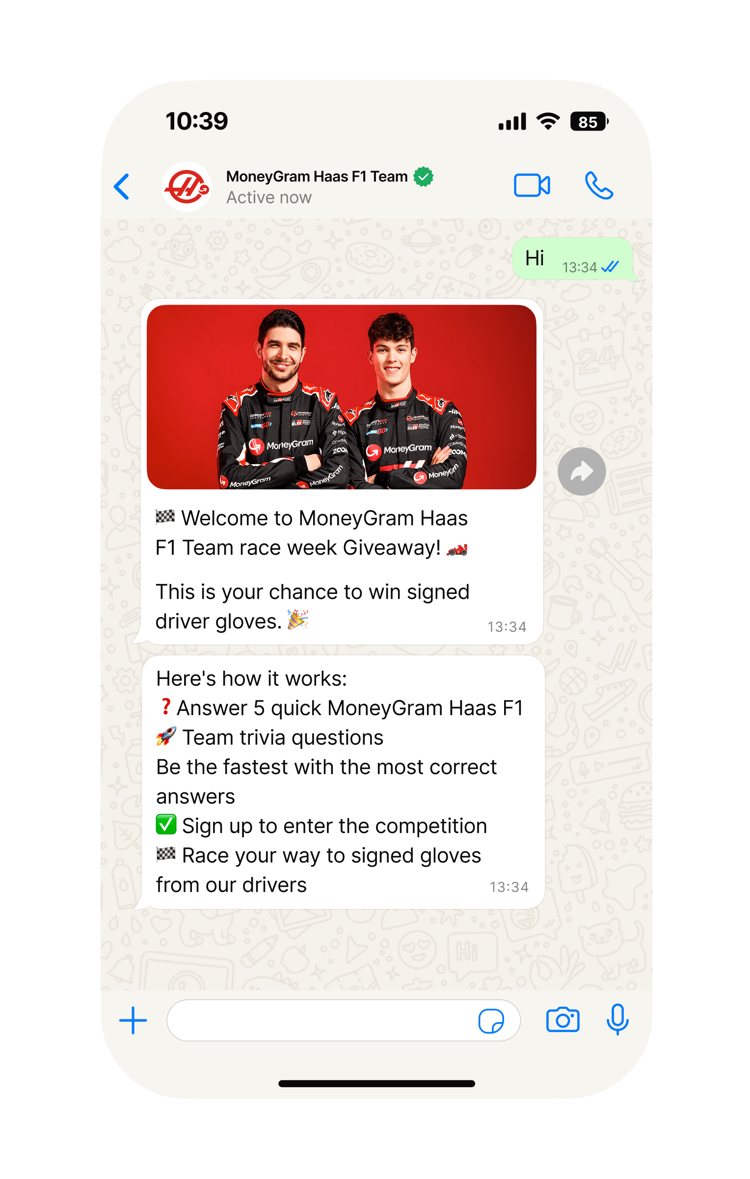Mobile phone screen showing a WhatsApp chat with “MoneyGram Haas F1 Team.” The team has sent an image of two racing drivers in black MoneyGram Haas F1 Team suits standing in front of a bright red background. Below, messages announce a “race week Giveaway” and a chance to win signed driver gloves, followed by instructions: answer five quick MoneyGram Haas F1 Team trivia questions, be the fastest with the most correct answers, sign up to enter the competition, and race your way to signed gloves.
