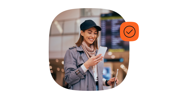 Woman at an airport looking at her phone with a checkmark icon, representing message status and RCS read receipts.