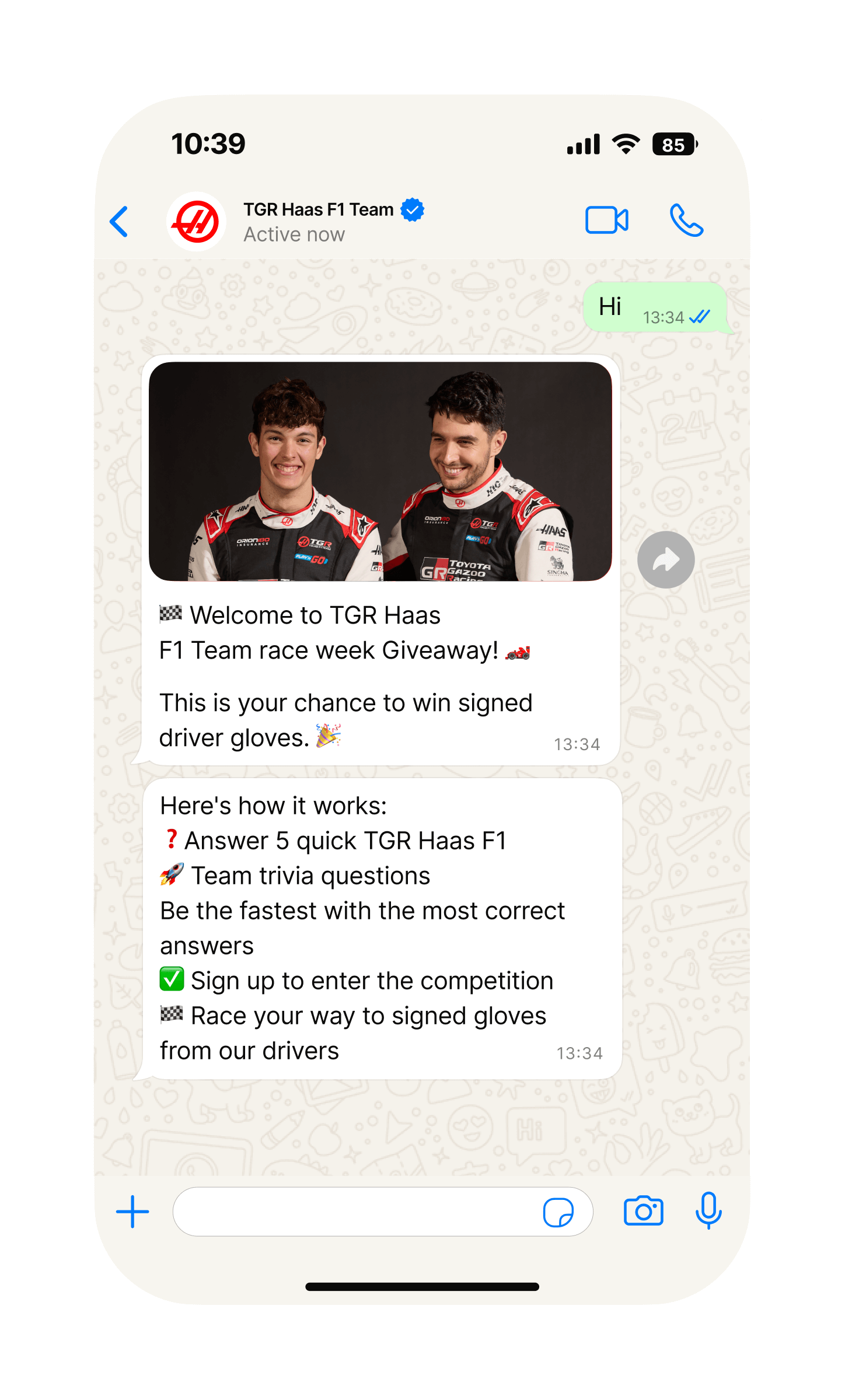 Mobile phone screen showing a WhatsApp chat with “TGR Haas F1 Team.” The team has sent an image of two racing drivers in black MoneyGram Haas F1 Team suits standing in front of a bright red background. Below, messages announce a “race week Giveaway” and a chance to win signed driver gloves, followed by instructions: answer five quick TGR Haas F1 Team trivia questions, be the fastest with the most correct answers, sign up to enter the competition, and race your way to signed gloves.