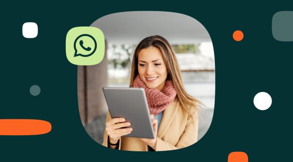 Smiling woman wearing a coat and scarf, standing outdoors and using a tablet, with a WhatsApp logo icon in a stylized frame on a dark green background.