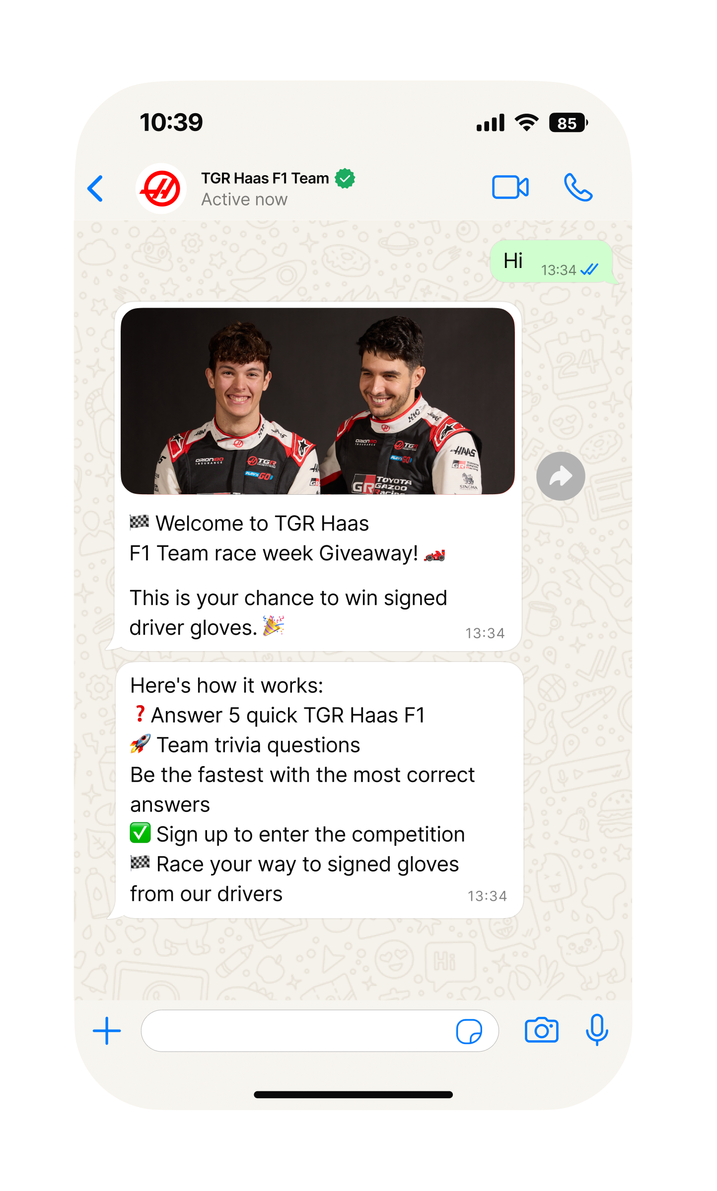 Mobile phone screen showing a WhatsApp chat with “TGR Haas F1 Team.” The team has sent an image of two racing drivers in black MoneyGram Haas F1 Team suits standing in front of a bright red background. Below, messages announce a “race week Giveaway” and a chance to win signed driver gloves, followed by instructions: answer five quick TGR Haas F1 Team trivia questions, be the fastest with the most correct answers, sign up to enter the competition, and race your way to signed gloves.
