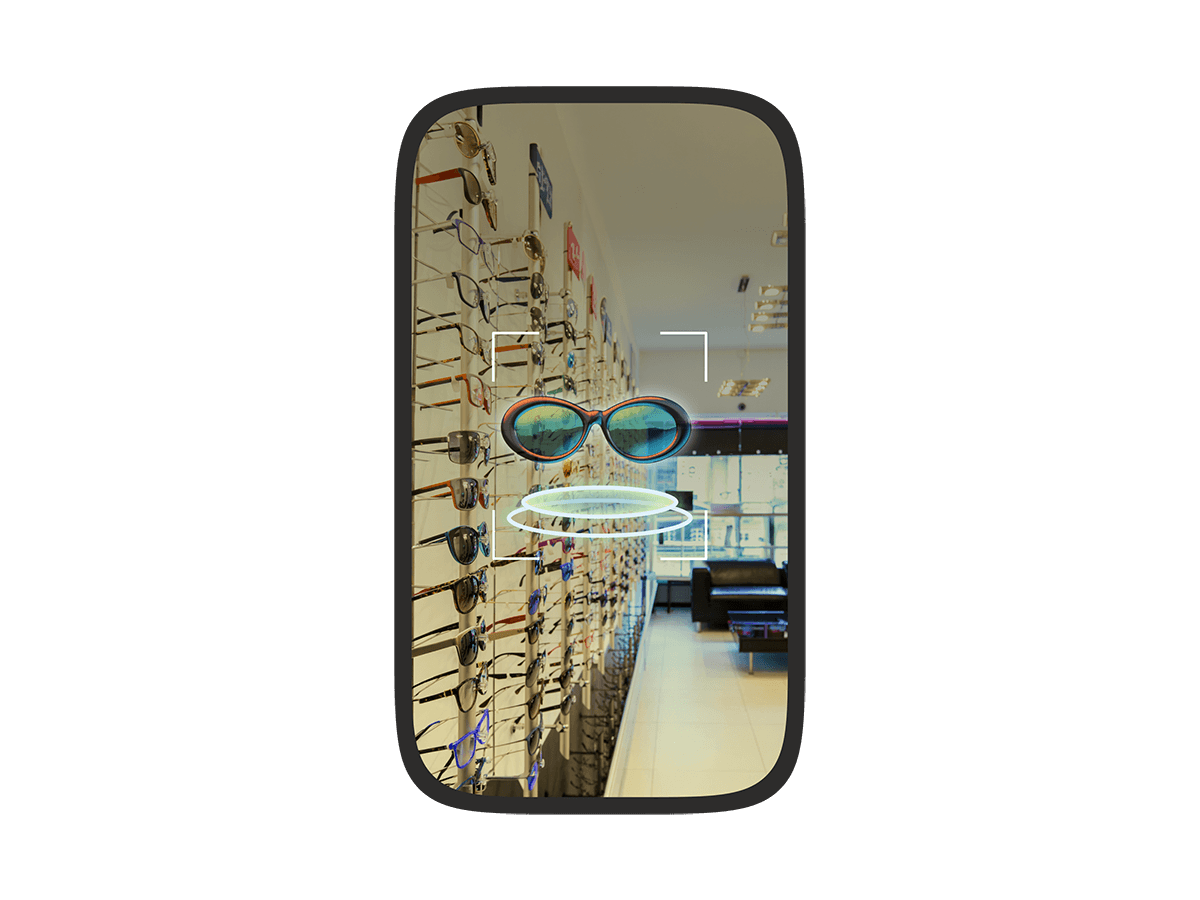 A phone screen showing an augmented reality view of an eyewear store with a virtual pair of sunglasses floating in the center, highlighted by a targeting frame.