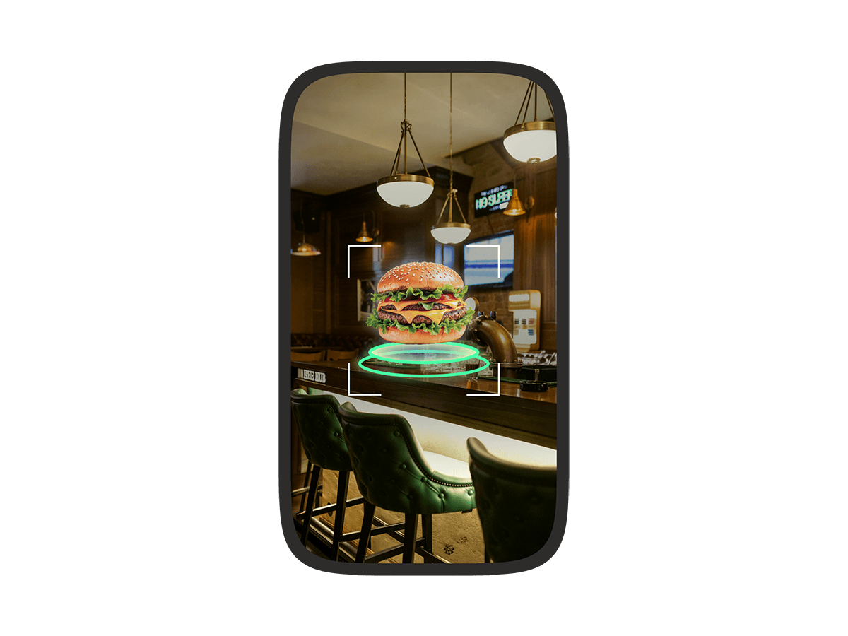 A phone screen showing an augmented reality view of a restaurant bar with a virtual burger floating on the counter, highlighted by a targeting frame.