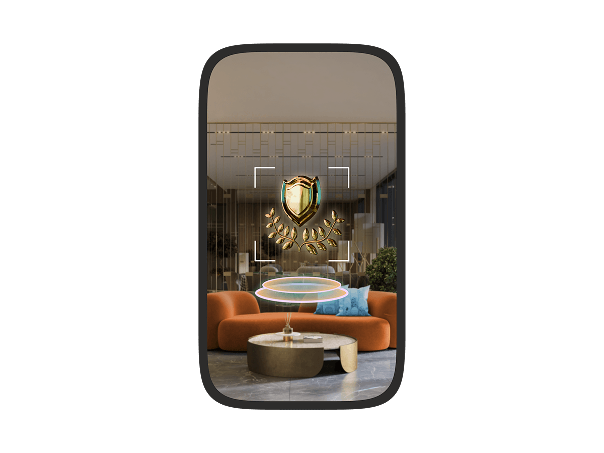 A phone screen showing an augmented reality view of a hotel lobby with a virtual gold shield and laurel wreath floating in the space, highlighted by a targeting frame.