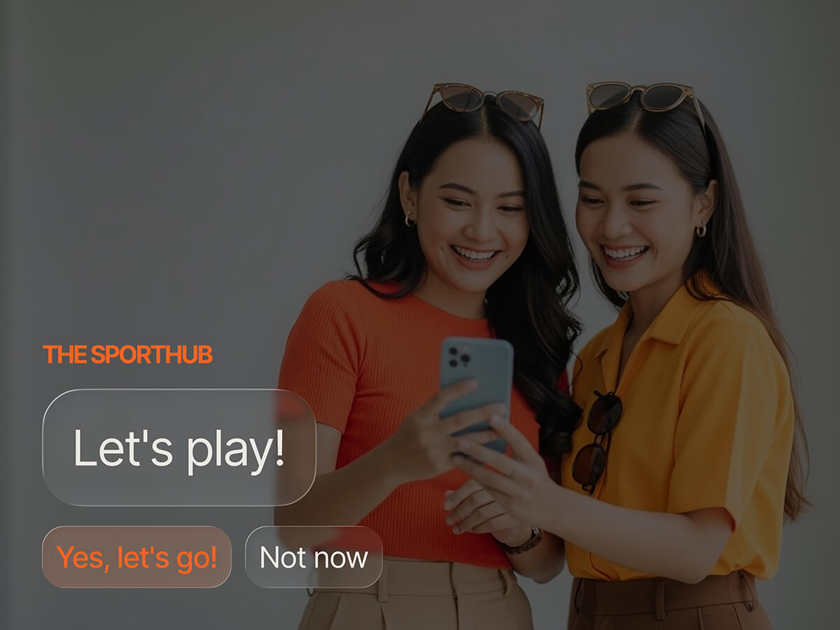 Two women laughing together over a phone showing a "Let's play!" gamification prompt from The SportHub, with "Yes, let's go!" and "Not now" options.