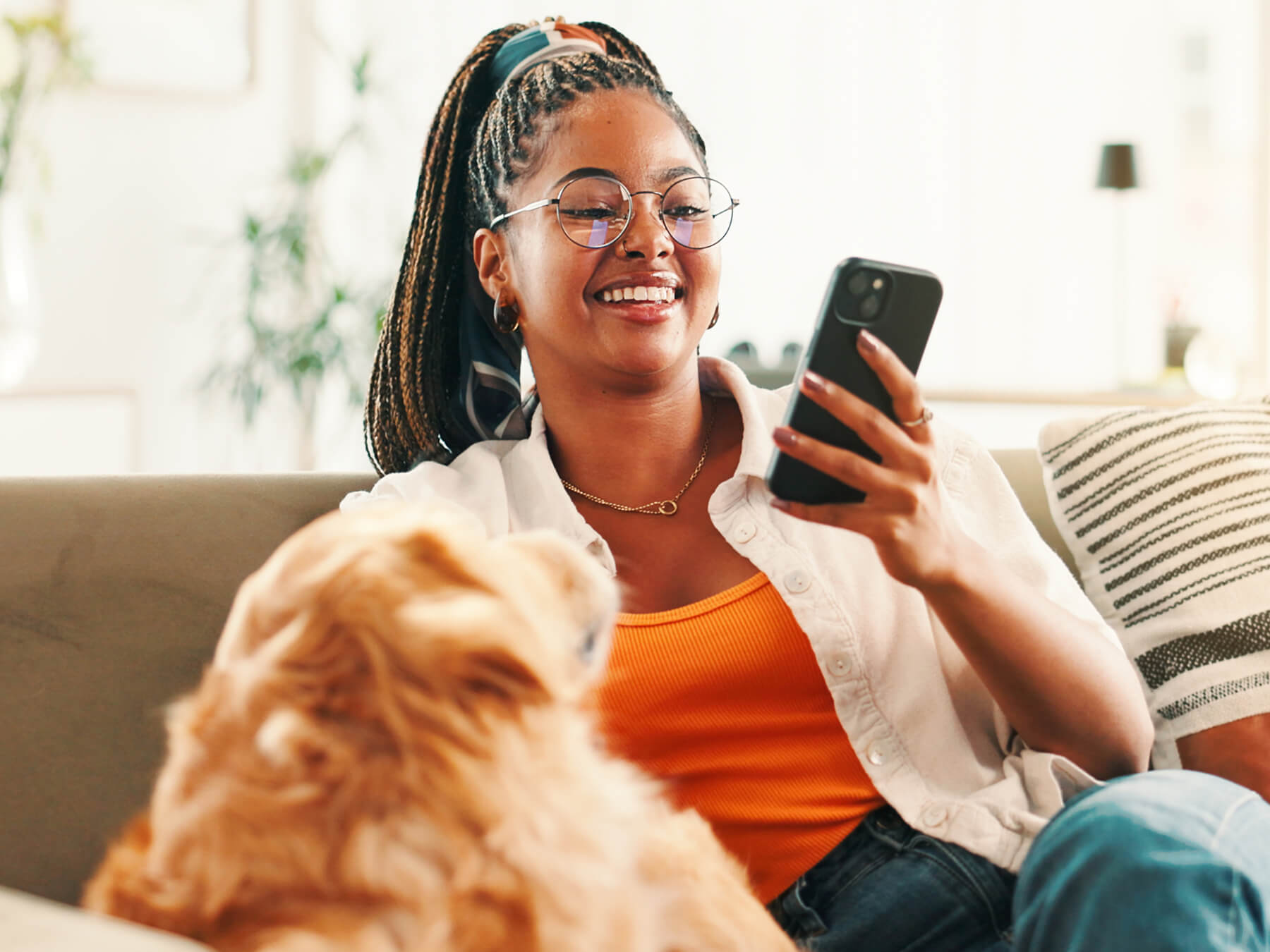 Woman on a sofa using a smartphone while a dog looks on.