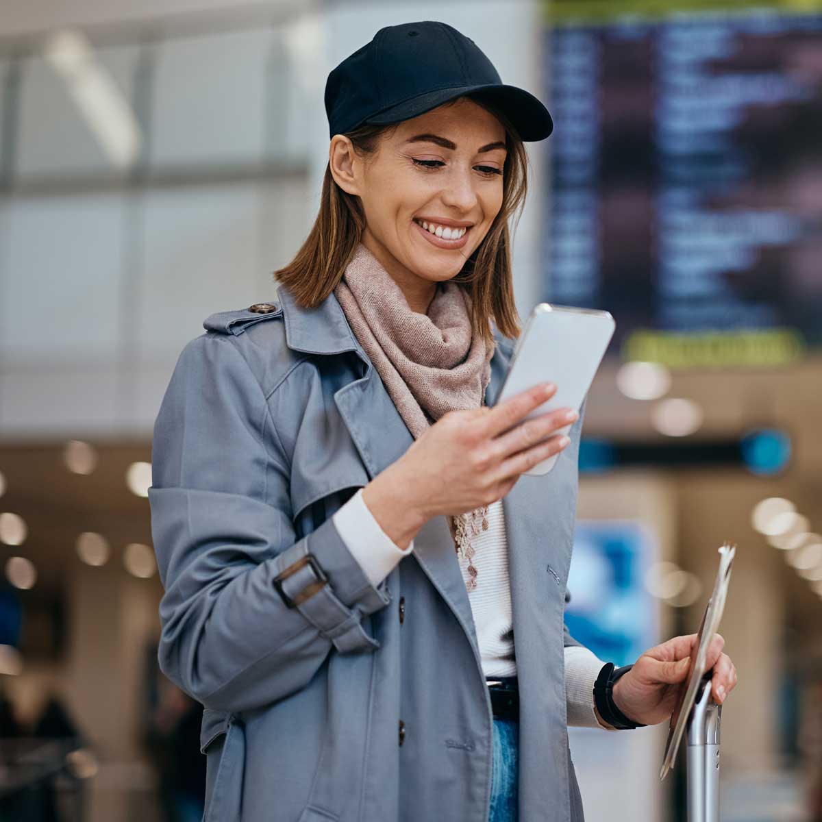 Woman at airport checking travel information on smartphone while holding boarding documents