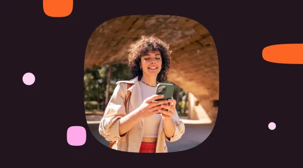 Woman smiling while using a smartphone outdoors under an arched structure.