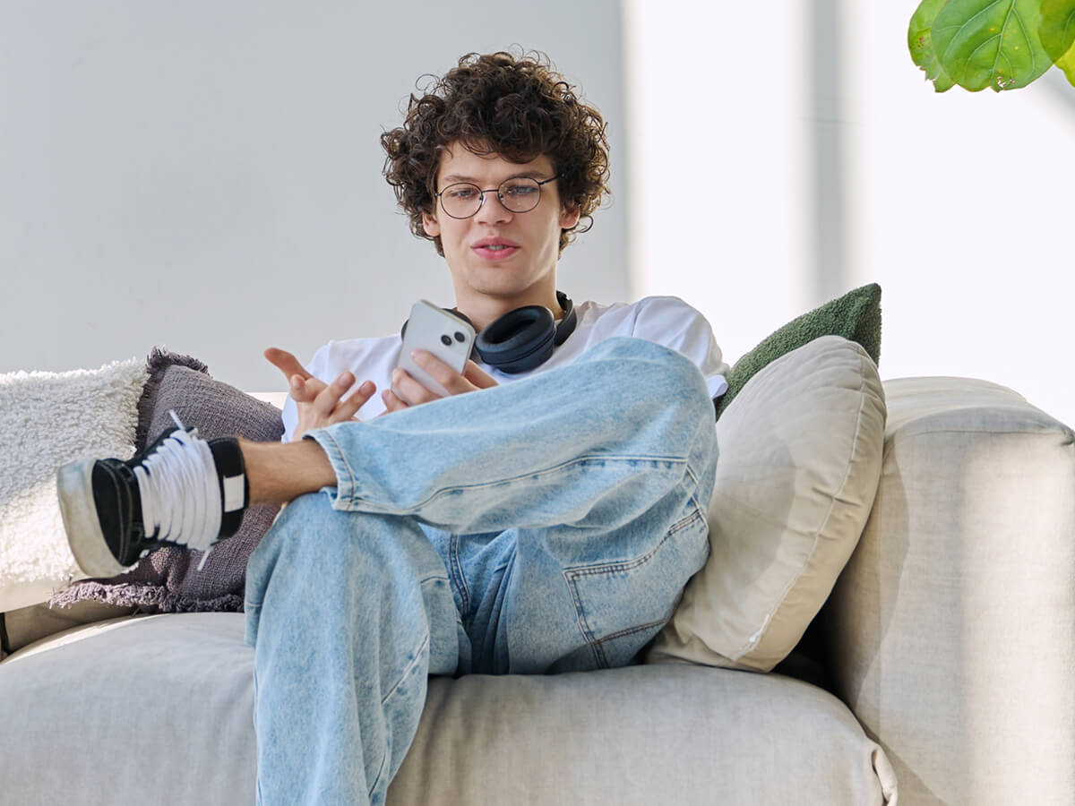 Person sitting on a sofa with headphones around their neck, using a smartphone at home.