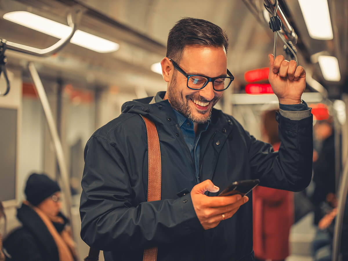 Man riding public transport and using a smartphone while holding an overhead strap.