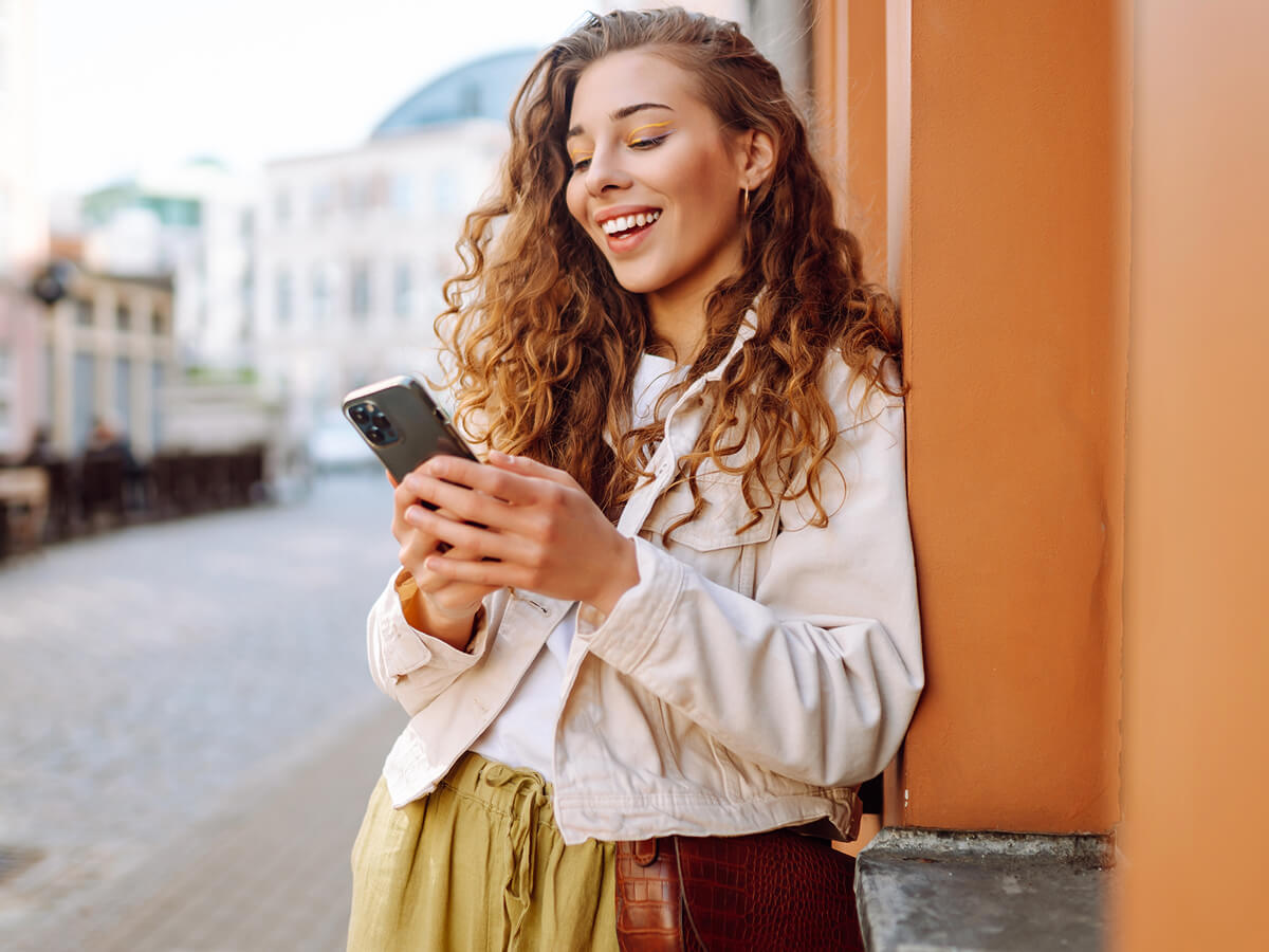 Woman leaning against a wall outdoors while checking her smartphone.