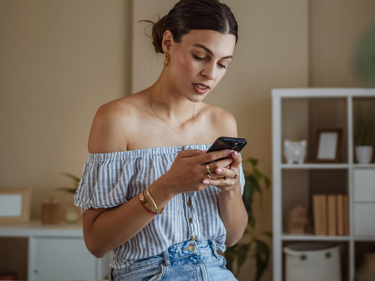 Woman standing indoors and using a smartphone.