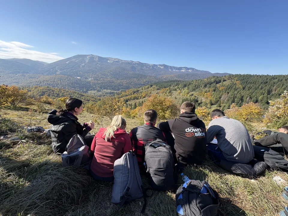 Bolt colleagues resting on a grassy ridge with backpacks, overlooking a mountain valley after the tree‑planting session organized by Mihai Tanase.