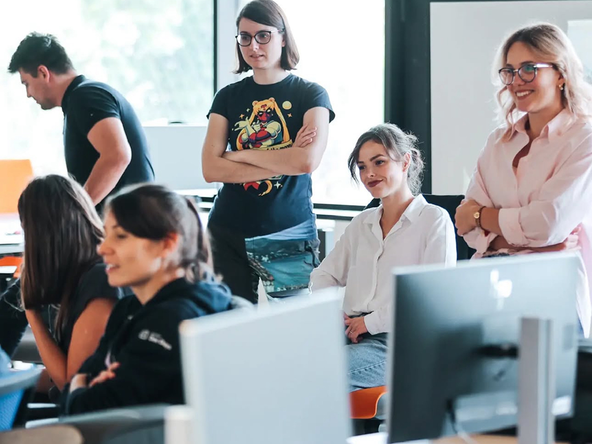 Team workshop in a bright meeting space with people gathered around computers and monitors